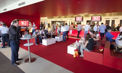 Guests gathered in a red-themed function lounge inside the stadium, with bar service, seating areas, and people socialising during an event.