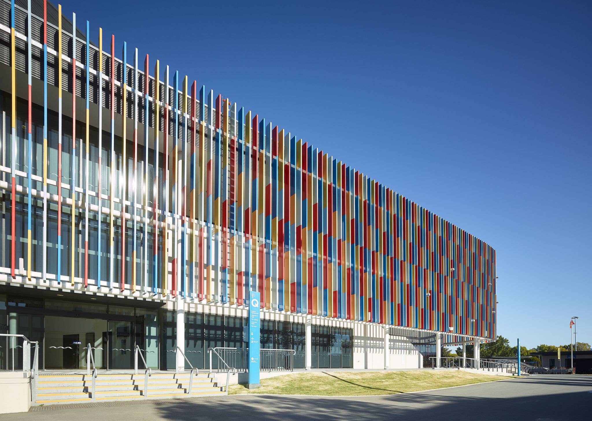 Exterior view of People First Stadium’s modern façade featuring colourful vertical panels and glass entry doors under a clear blue sky.
